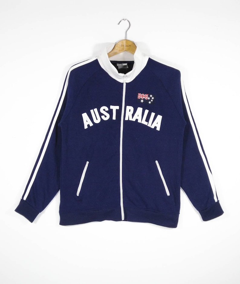 May include: A navy blue zip-up jacket with white stripes down the sleeves and white lettering that says "AUSTRALIA" with the Australian flag above the word.
