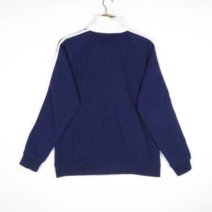 May include: A navy blue zip-up sweatshirt with white stripes on the sleeves. The sweatshirt has a high collar and a relaxed fit.