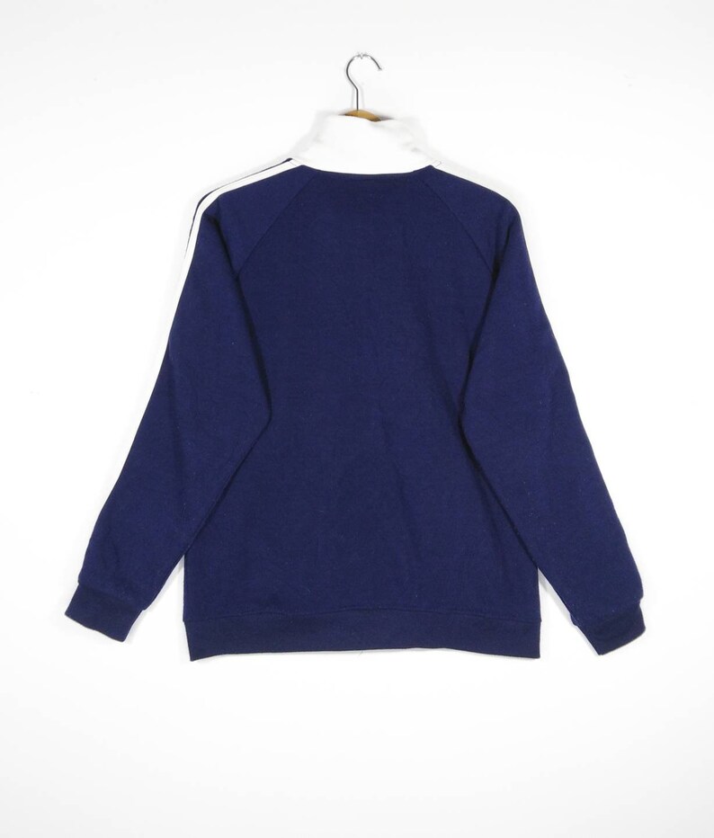 May include: A navy blue zip-up sweatshirt with white stripes on the sleeves. The sweatshirt has a high collar and a relaxed fit.