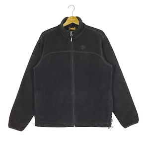 K&ouml;nnte beinhalten: Eine schwarze Fleecejacke mit Rei&szlig;verschluss und einem kleinen Logo auf der linken Brust.
