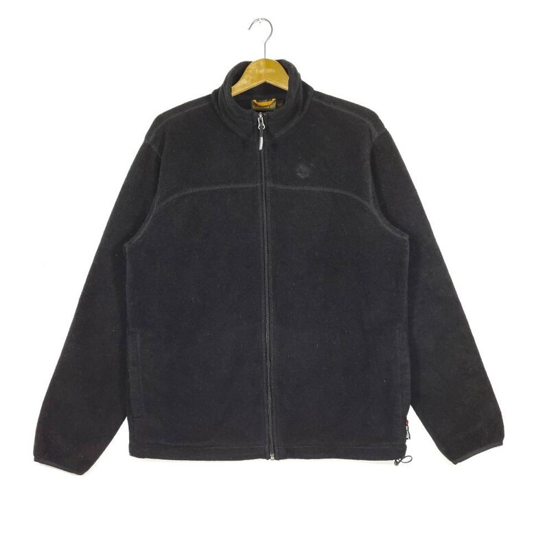 K&ouml;nnte beinhalten: Eine schwarze Fleecejacke mit Rei&szlig;verschluss und einem kleinen Logo auf der linken Brust.