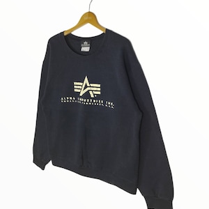 May include: A black Alpha Industries sweatshirt with a gold star logo and the text "ALPHA INDUSTRIES INC. KNOXVILLE, TENNESSEE, U.S.A."