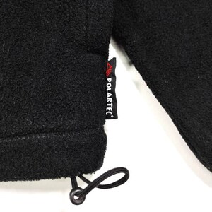 K&ouml;nnte beinhalten: Schwarze Fleecejacke mit schwarzem Kordelzug und rotem "POLARTEC"-Etikett.