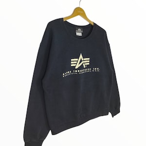May include: A dark blue Alpha Industries sweatshirt with a white logo featuring a stylized airplane wing and the text "Alpha Industries Inc. Knoxville, Tennessee, U.S.A."