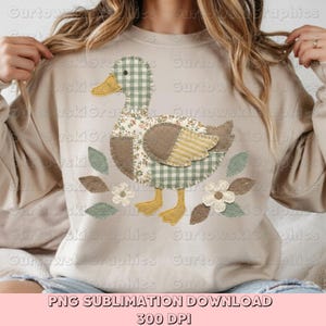 May include: A beige sweatshirt featuring a patchwork duck design. The duck has a checkered green and white head, floral and striped wings, and yellow feet. The design includes leaves and flowers. Text at the bottom reads "PNG SUBLIMATION DOWNLOAD 300 DPI."