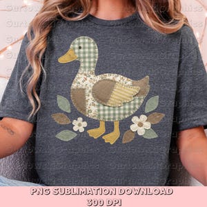 May include: Dark gray t-shirt featuring a patchwork duck design. The duck has a checkered head, floral body, and striped wings. The design includes leaves and flowers. Text at the bottom reads "PNG SUBLIMATION DOWNLOAD 300 DPI".