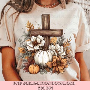 May include: Beige t-shirt featuring a wooden cross design with a white pumpkin, orange pumpkins, and flowers. The design includes fall foliage and the text "PNG SUBLIMATION DOWNLOAD 300 DPI".
