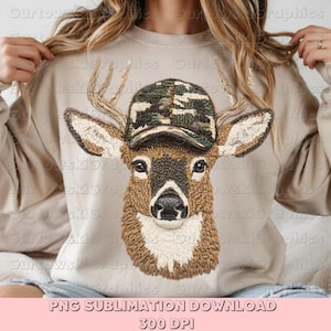 May include: A beige sweatshirt featuring an embroidered deer head wearing a camouflage baseball cap. The deer has large antlers and a detailed, textured design. The text "PNG SUBLIMATION DOWNLOAD 300 DPI" is at the bottom.