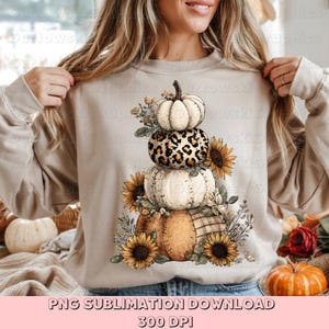 May include: Beige sweatshirt featuring a stacked pumpkin design with sunflowers and fall foliage. The design includes pumpkins with leopard print, white, and plaid patterns. Text at the bottom reads "PNG SUBLIMATION DOWNLOAD 300 DPI."