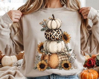 May include: Beige sweatshirt featuring a stacked pumpkin design with sunflowers and fall foliage. The design includes pumpkins with leopard print, white, and plaid patterns. Text at the bottom reads "PNG SUBLIMATION DOWNLOAD 300 DPI."