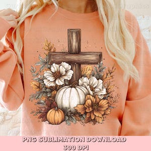 May include: A peach-colored sweatshirt featuring a graphic of a wooden cross surrounded by white and orange flowers, pumpkins, and fall foliage. The design includes the text "PNG SUBLIMATION DOWNLOAD" and "300 DPI".