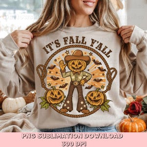 Könnte beinhalten: Beiges Sweatshirt mit einem Herbst-Themen-Grafik. Das Design zeigt einen Kürbiskopf-Cowboy mit dem Text "It's Fall Y'all" in einem kreisförmigen Seilrahmen, umgeben von Fledermäusen, Sternen und Kürbissen. Der untere Teil des Bildes lautet "PNG SUBLIMATION DOWNLOAD 300 DPI".