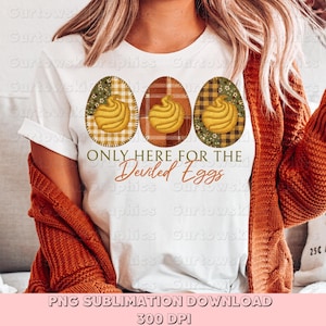 Puede incluir: Camiseta blanca con tres diseños de huevos de Pascua con gráficos de huevos rellenos. Los huevos tienen patrones de cuadros y florales. El texto "ONLY HERE FOR THE Deviled Eggs" está debajo.