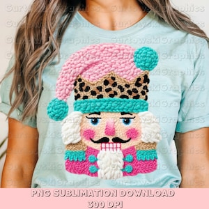 May include: A light blue t-shirt featuring a colorful, detailed nutcracker design. The nutcracker has a pink hat with a leopard print band, a turquoise brim, and a pink and turquoise body. The text "PNG SUBLIMATION DOWNLOAD 300 DPI" is at the bottom.