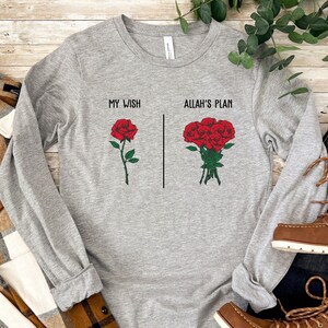 May include: Gray long-sleeve t-shirt with the text "My Wish" and a single red rose on the left side and "Allah's Plan" with a bouquet of red roses on the right side.
