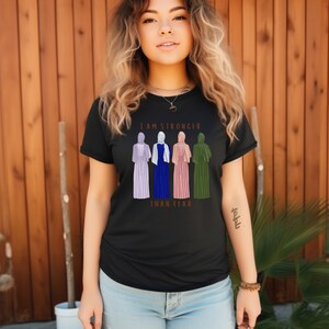 Peut inclure: T-shirt noir avec un graphique de quatre femmes portant des foulards et le texte "Je suis plus forte que la peur".