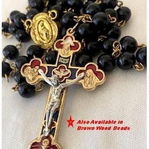 May include: A rosary with black beads and gold-colored metal accents. The cross features a silver figure of Jesus and red, blue, and gold details. The text "Also Available in Brown Wood Beads" is visible.