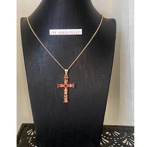 Op de afbeelding: Een gouden ketting met een rode kristallen kruis hanger. De hanger is gemaakt van 18 karaat verguld.