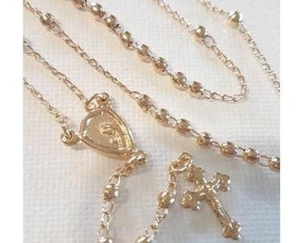 Puede incluir: Un collar de rosario dorado con un colgante en forma de corazón y un pequeño dije en forma de cruz.