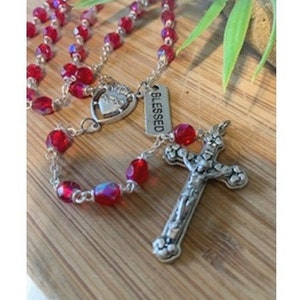 Rosenkrans med rubinfärgad födelsesten, rosenkrans med födelsesten i juli i röd rubin med etikett med födelsestensattribut och häfte med hur man ber rosenkransen, Sacred Heart