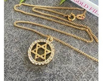 Op de afbeelding: Een gouden ketting met een hanger in de vorm van een Davidster, versierd met heldere kristallen rond de rand. De hanger zit aan een gouden ketting met een karabijnhaak.