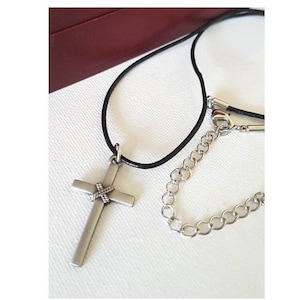 May include: A silver cross pendant with a braided design hangs from a black leather cord necklace. A silver chain is also included.
