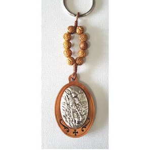 May include: A wooden keychain featuring a silver metal image of Saint Michael the Archangel. The keychain has a brown cord with a circle of wooden beads.