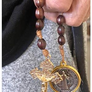 May include: A brown wooden rosary with a gold-colored cross and a round medal featuring a saint. The medal has the words "Sancta Maria" and "Ora Pro Nobis" inscribed on it.