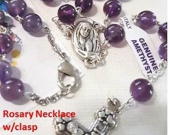 May include: A purple amethyst rosary necklace with a silver clasp and a silver crucifix with a heart design. The tag reads "Genuine Amethyst, Italy".