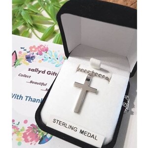 Puede incluir: Un collar con una cruz de plata en una caja de terciopelo negro con una etiqueta blanca que dice "Sterling Medal".
