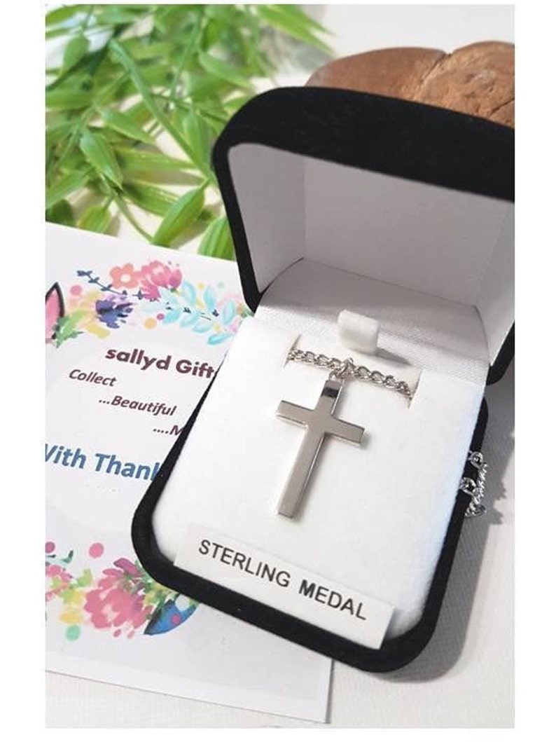 Puede incluir: Un collar con una cruz de plata en una caja de terciopelo negro con una etiqueta blanca que dice "Sterling Medal".