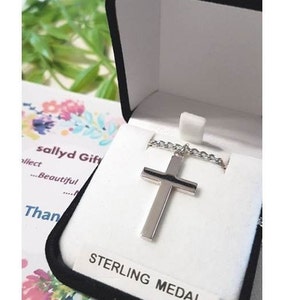 Puede incluir: Un collar con una cruz de plata en una caja de terciopelo negro con una etiqueta blanca que dice "STERLING MEDAL".