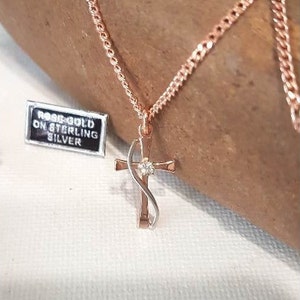 Könnte beinhalten: Halskette mit Kreuzanhänger aus Roségold und kleinem Diamanten in der Mitte. Das Kreuz hängt an einer filigranen Kette. Ein kleines Etikett zeigt "ROSE GOLD ON STERLING SILVER".