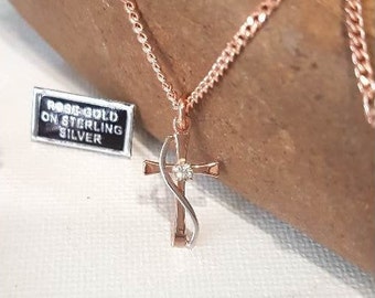 Puede incluir: Collar con colgante de cruz de oro rosa y un pequeño diamante en el centro. La cruz está en una cadena delicada. Una pequeña etiqueta indica "ROSE GOLD ON STERLING SILVER".