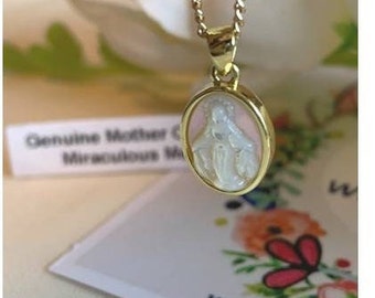 Op de afbeelding: Gouden ketting met een hanger met een wit beeld van de Maagd Maria op een roze achtergrond. De hanger is ovaalvormig en heeft een gouden rand.