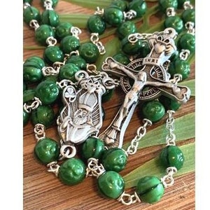 May include: Green rosary beads with a silver crucifix and a silver charm of a saint. The crucifix has the word "INRI" on it.