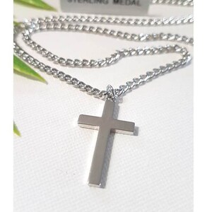 Puede incluir: Un collar de cadena de plata con un colgante de cruz de plata. La cadena es de estilo curb chain. La etiqueta en la cadena dice "Sterling Medal".