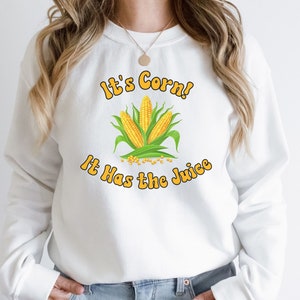 May include: White sweatshirt with a graphic of corn on the cob and the text "It's Corn! It Has the Juice" in yellow and orange letters.