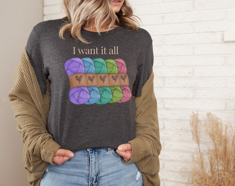 May include: A dark gray t-shirt with the text "I want it all" and a graphic of colorful yarn balls with hearts.