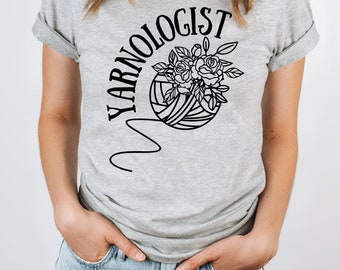 May include: A gray t-shirt with the text "YARNOLOGIST" in a black circular arc above a black and white illustration of a ball of yarn with roses.