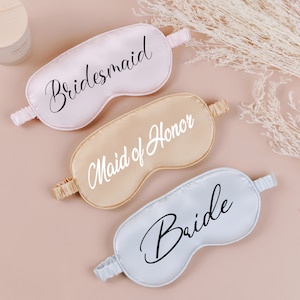 May include: Three satin sleep masks with the words "Bride", "Maid of Honor", and "Bridesmaid" written in black script.