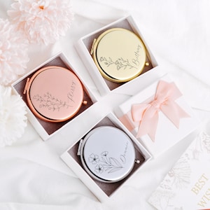 May include: Three round compact mirrors with personalized names, "Brittany", "Libby", and "Dominque", engraved on the front. Each mirror is in a white box with a floral design.