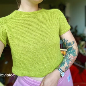 A relaxed fit knitted tee knitting in green worsted weight cotton yarn worn on a female model with tattoos.
