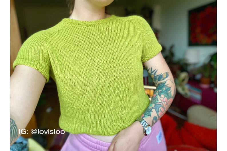 A relaxed fit knitted tee knitting in green worsted weight cotton yarn worn on a female model with tattoos.