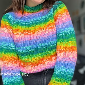 May include: A rainbow striped knitted sweater with a crew neck. The sweater is made with a soft, colorful yarn. IG: @madebybusby