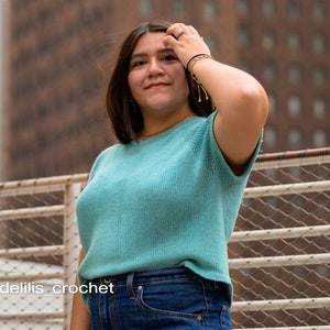 A relaxed fit knitted tee knitting in a fingering weight blue yarn worn on a female model standing in a city.