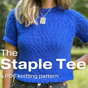 A relaxed fit knitted tee knitting in worsted weight blue yarn worn on a female model who is standing outside. TEXT: The Staple Tee, a PDF knitting pattern