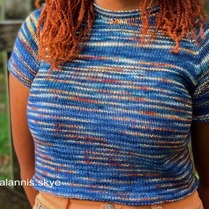 A relaxed fit knitted tee knitting in blue, orange, and white yarn worn on a female model outside.