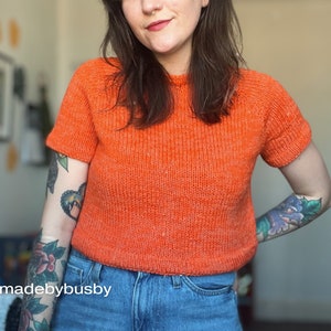 A relaxed fit knitted tee knitting in orange yarn worn on a female model with tattoos and piercings.