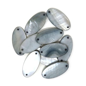 May include: A group of ten oval-shaped, grey mother of pearl shell beads with two small black holes in each bead.